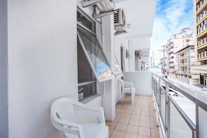 Uma varanda com cadeiras brancas, uma janela e vista para um edifício de hotel.