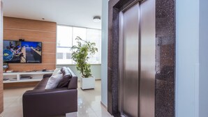 Una sala de estar moderna con un sofá, un televisor de pantalla plana, una planta en maceta y un amplio ventanal corredizo.