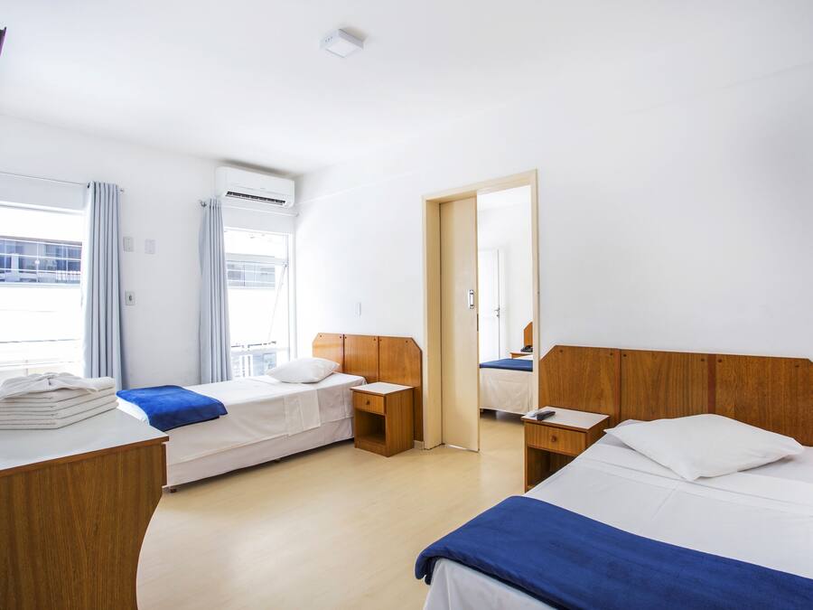 A hotel room with two beds, a wooden desk, a bedside table, and a window with curtains.