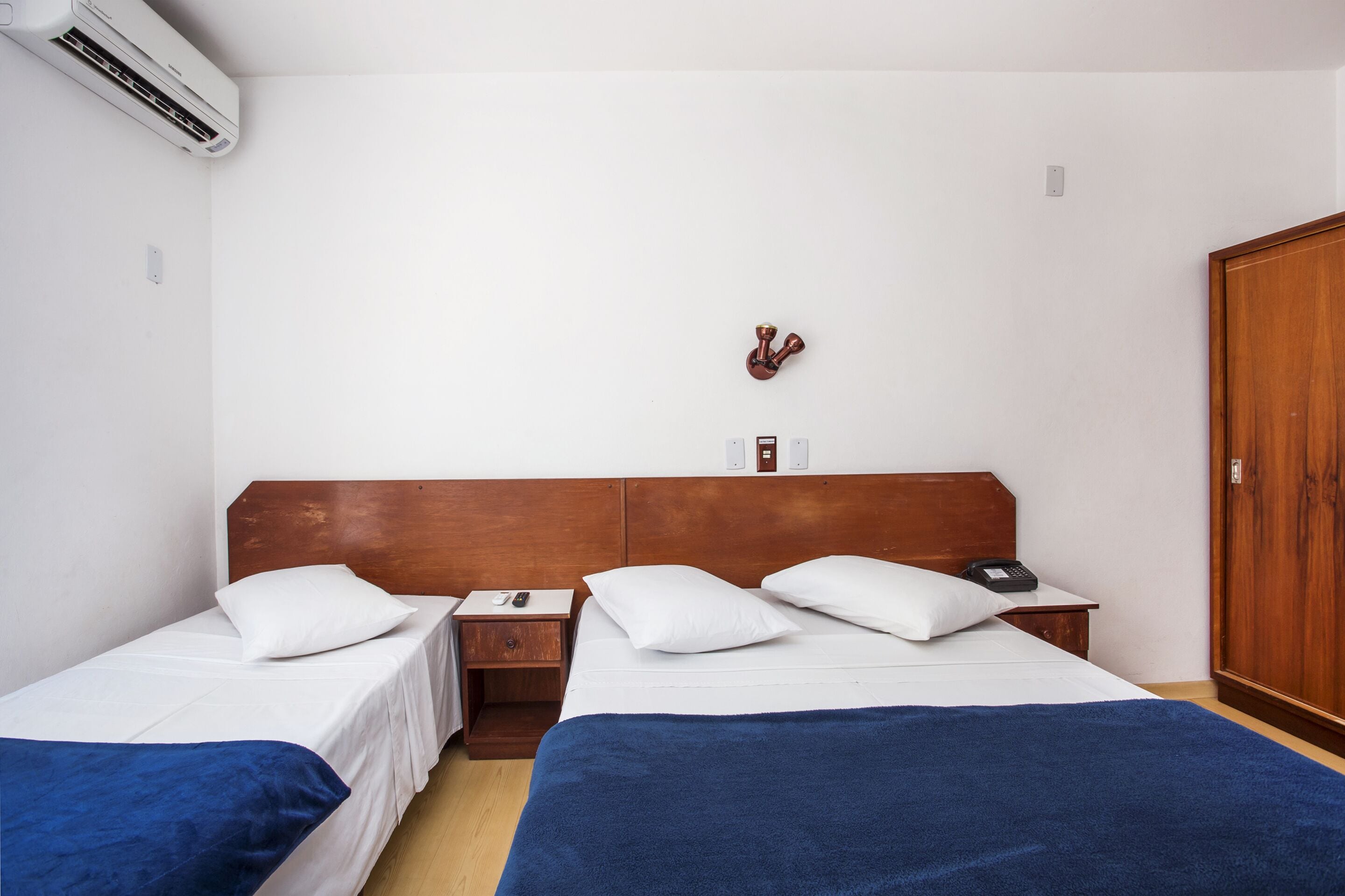 Een hotelkamer met twee eenpersoonsbedden, een houten hoofdbord, een nachtkastje met een telefoon en een kledingkast.