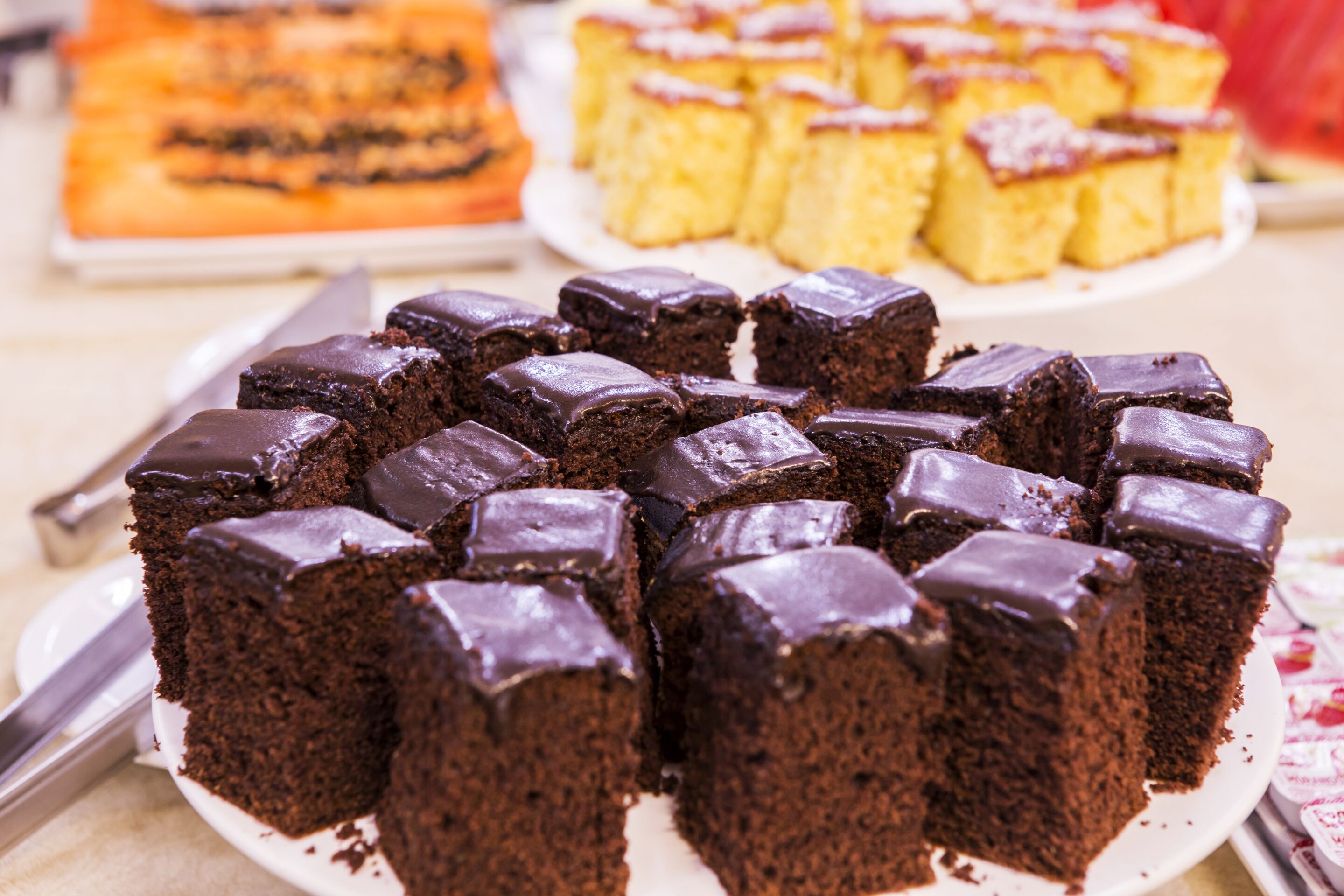 A variety of cakes on a table, including chocolate and yellow sponge cakes.