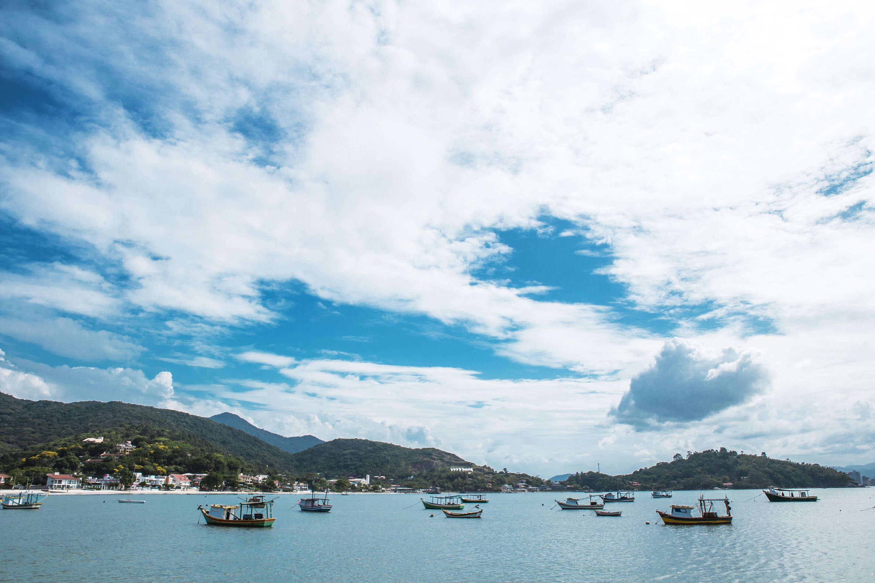 A coastal scene with several boats on calm water, a mountainous backdrop, and a clear sky.