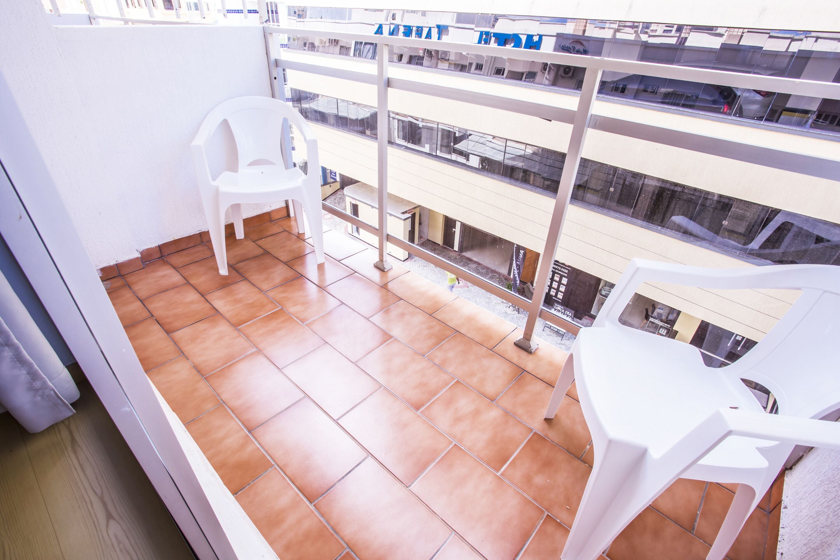 A balcony with terracotta tiles, white plastic chairs, and a metal railing.