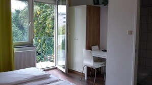A bedroom with a bed, a desk, and a chair. There is a window with a view of trees and buildings. - Hotel - Restaurant Valley Rose (Vienna)