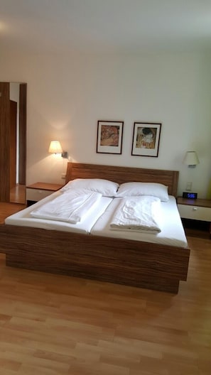 Una cama doble impecable con cabecera de madera en una habitación de hotel. Hay dos mesitas de noche, cada una con una lámpara. Dos cuadros enmarcados están colgados en la pared sobre la cama.