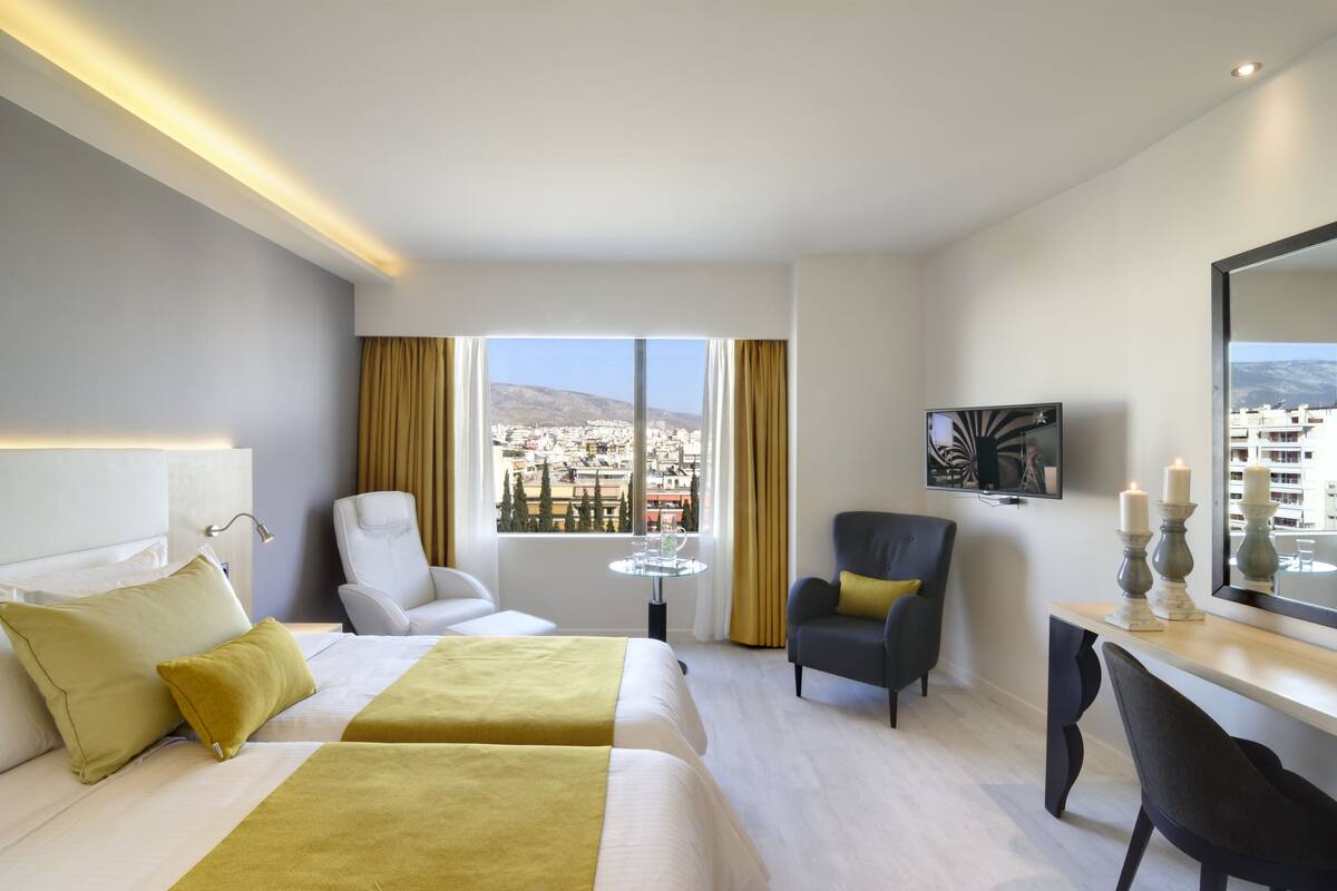 A hotel room with two beds, a desk, a chair, a TV, and a window with a city view.