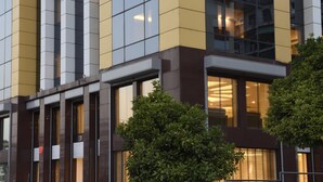 Un edificio moderno con amplios ventanales y paneles de fachada en tonos amarillo y marrón.