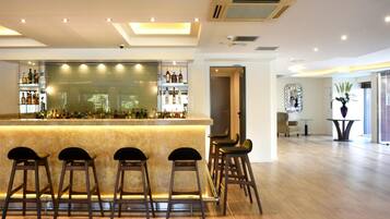 Una zona de bar con mostrador, taburetes y estantes llenos de botellas.