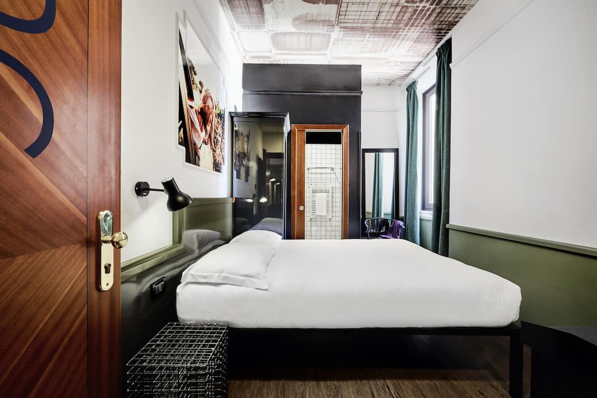 A hotel room with a bed, a desk, a chair, a mirror, and a window with curtains.