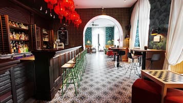 A bar area with a long counter, green bar stools, and a variety of bottles. There is a checkered table and red seating in the foreground.