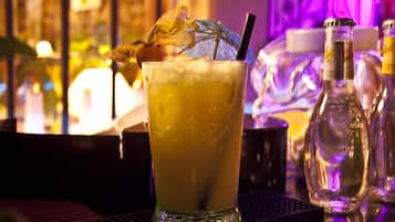 A cocktail with a straw and garnish on a bar counter, surrounded by bottles and glasses.