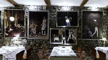 A restaurant with stone walls and framed black-and-white photographs. Tables are set with white tablecloths and silverware.