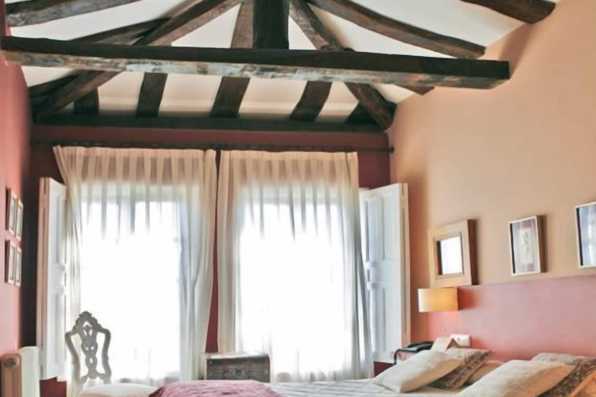 Un dormitorio con una cama grande, una silla, una mesita de noche y una ventana con cortinas.