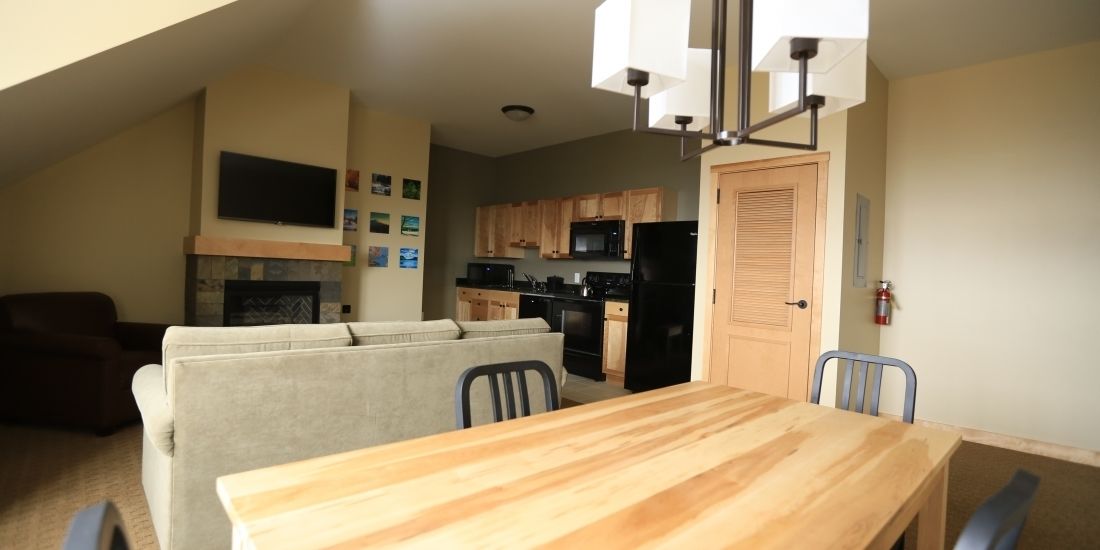 A compact living space with a sofa, dining table, kitchen area, and a TV mounted on the wall.