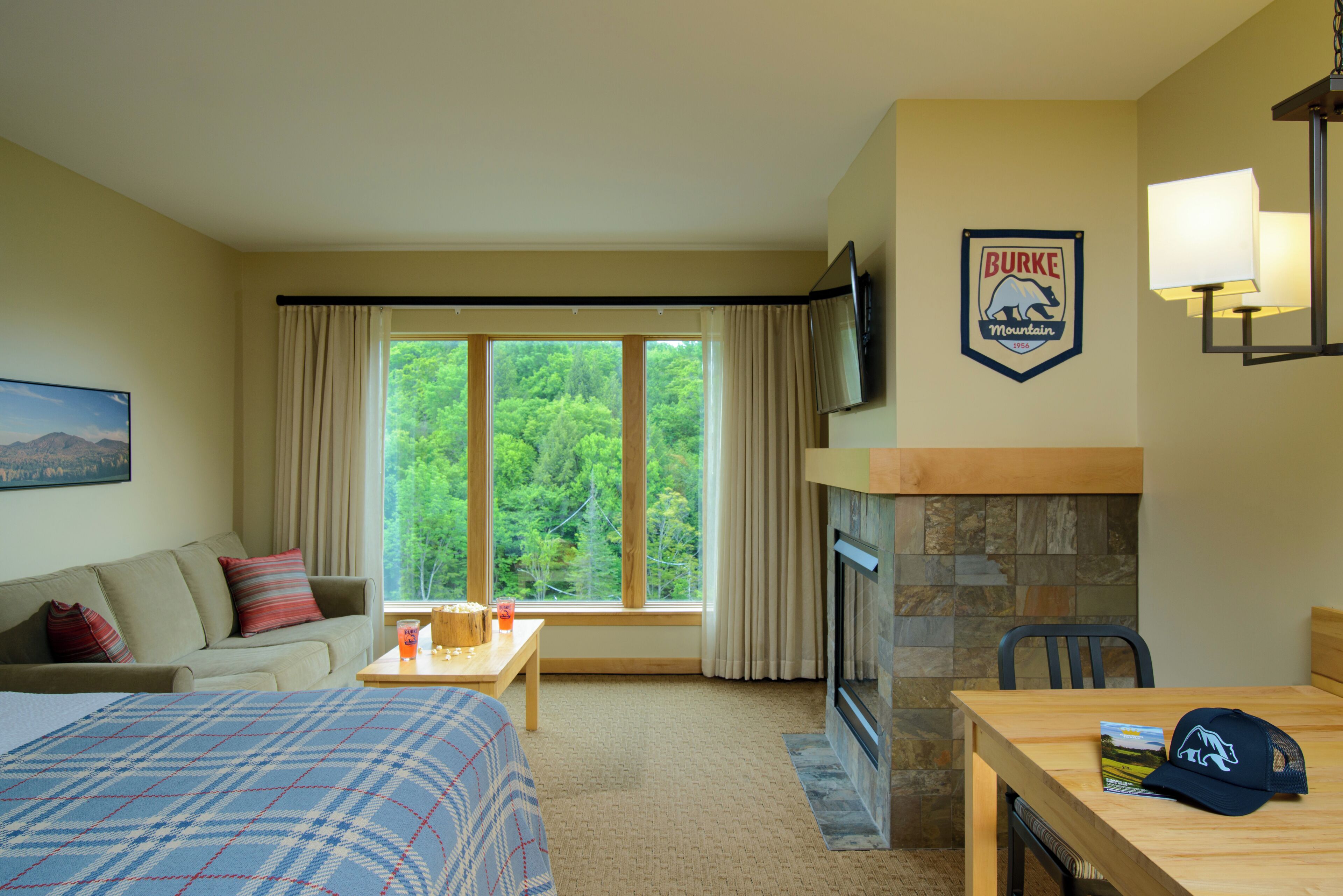 Ett hotellrum med en säng, en soffa, ett matbord, en öppen spis, en tv och ett fönster med gardiner.
