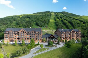 Un gran lodge con varios pisos y balcones, rodeado por un césped cuidado y una pista de esquí al fondo.