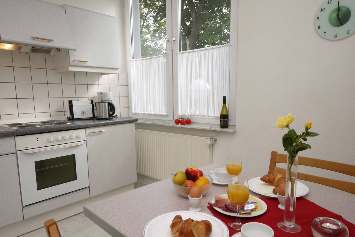 Una cocina con armarios blancos, una estufa y un ventanal con cortinas.