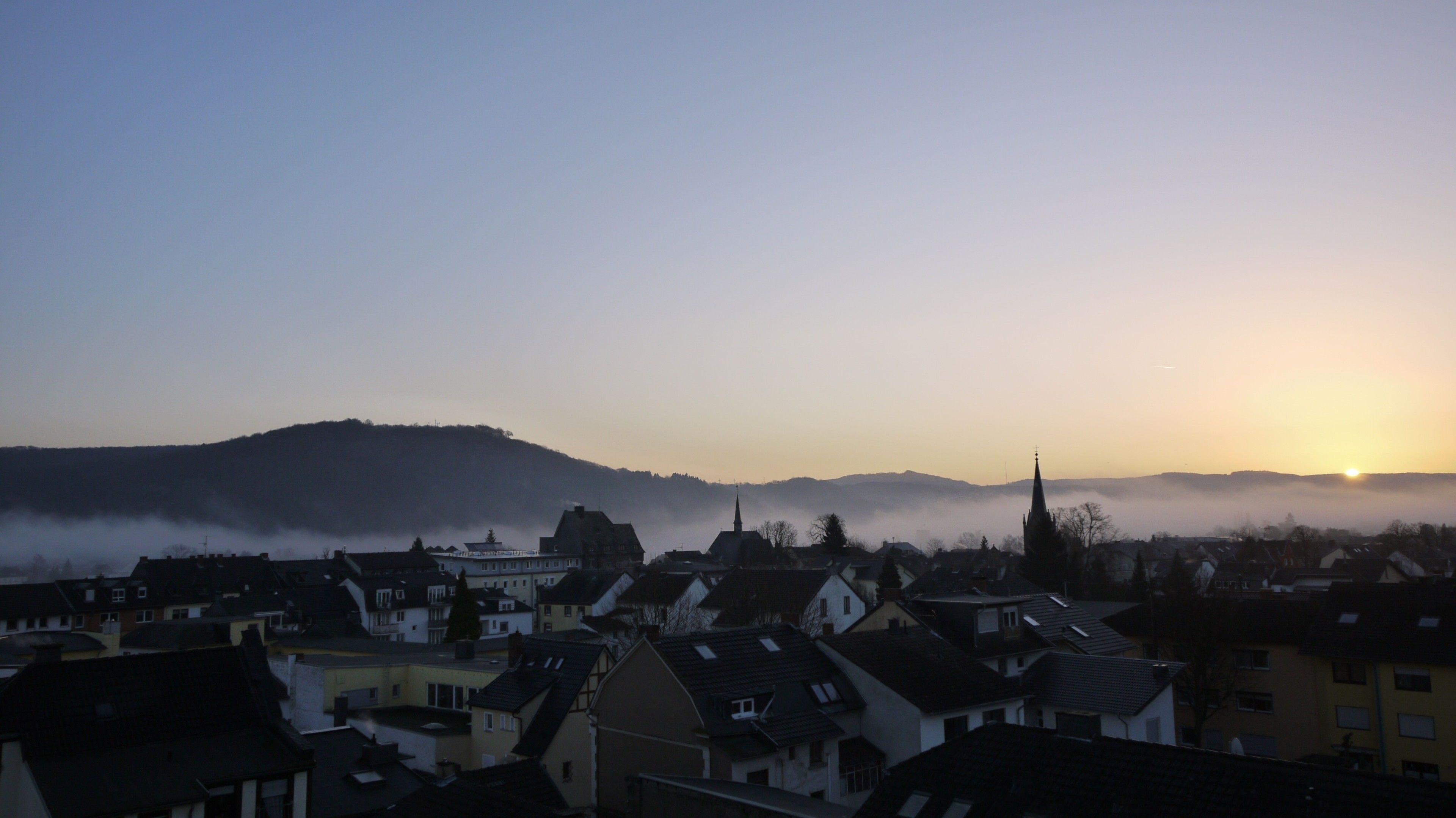 A town with buildings and a church spire silhouetted against a sunrise.