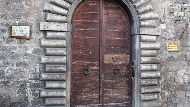 A large, arched wooden door with metal handles and a sign above it.