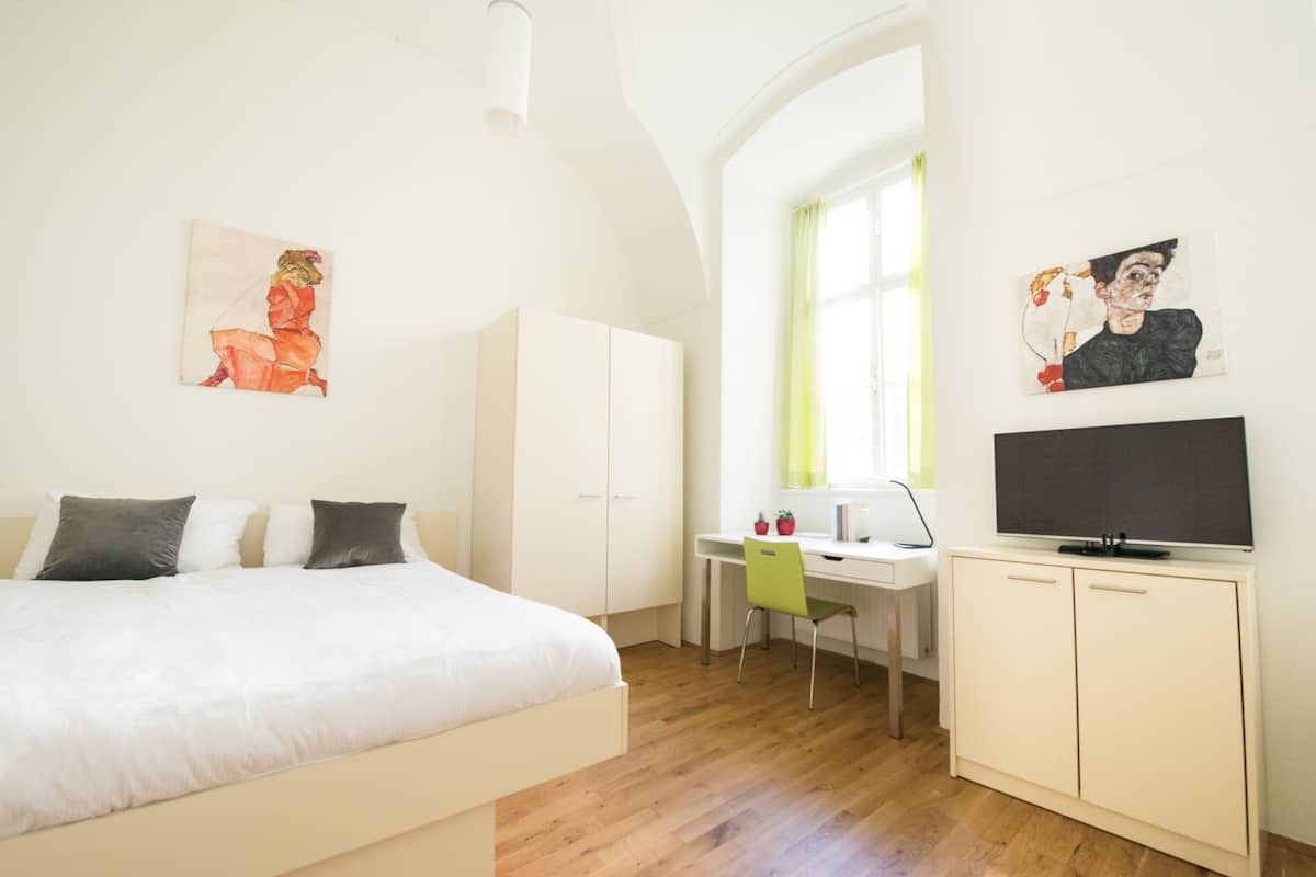 Una camera da letto con un letto, una scrivania, una sedia, una televisione e opere d'arte alle pareti.