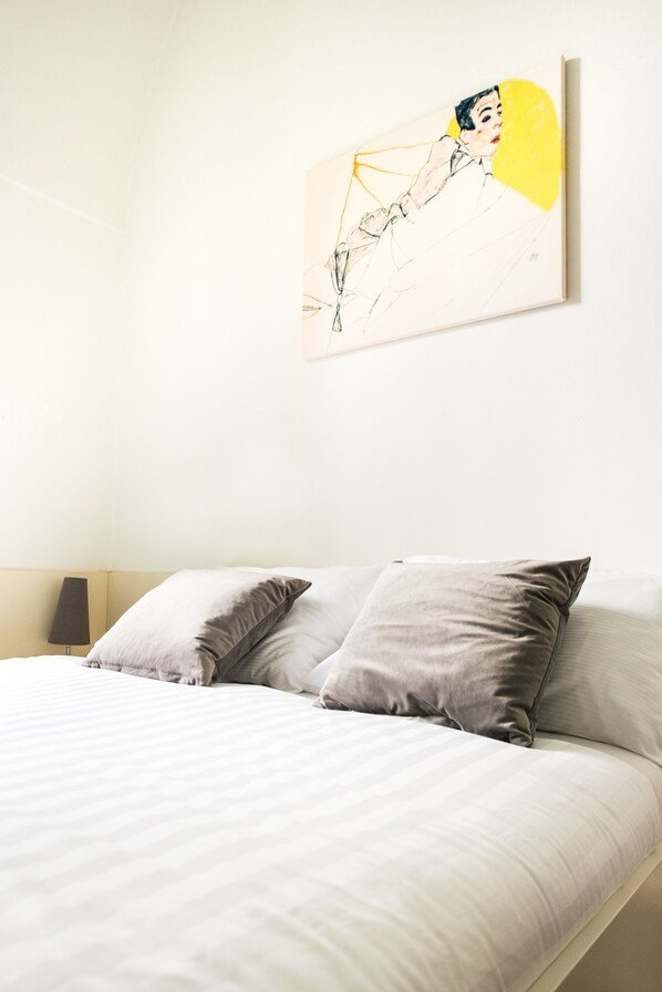 A neatly made bed with two pillows, a bedside lamp, and a wall-mounted painting.
