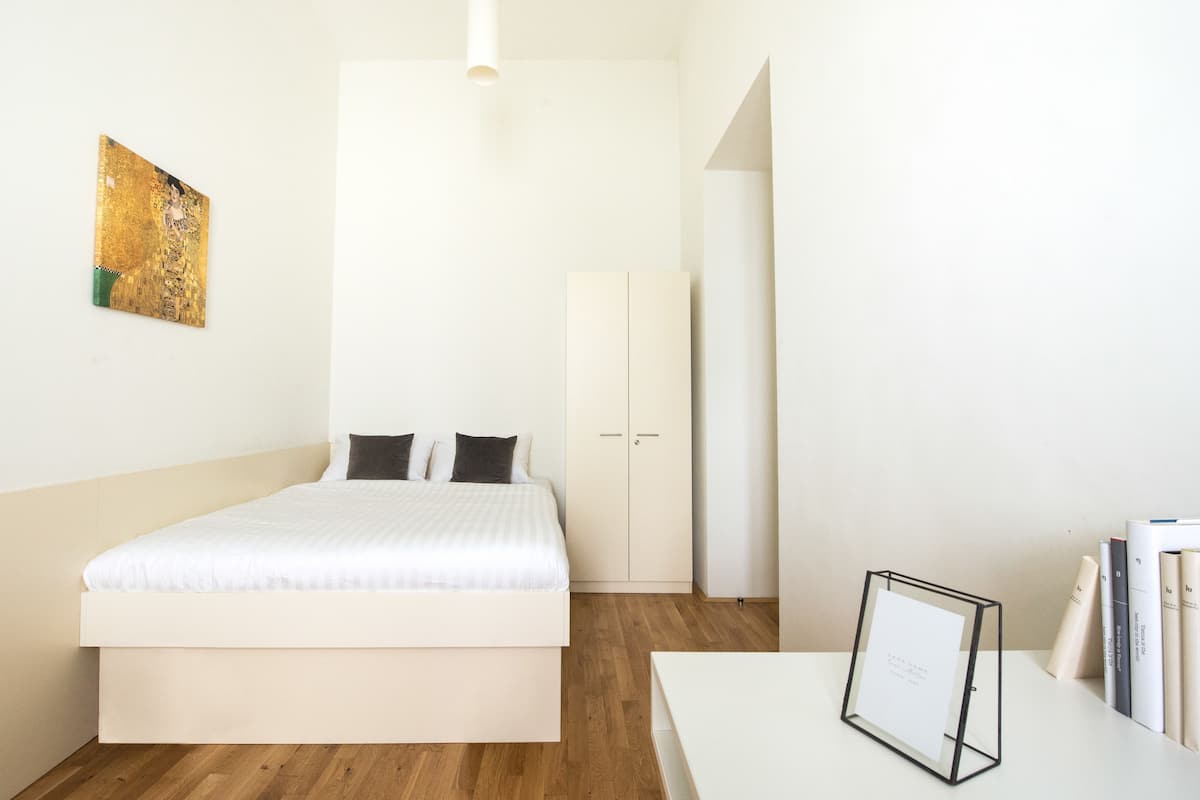 Una camera d'albergo dal design minimalista con un letto grande, un armadio bianco e un quadro incorniciato su un tavolino.