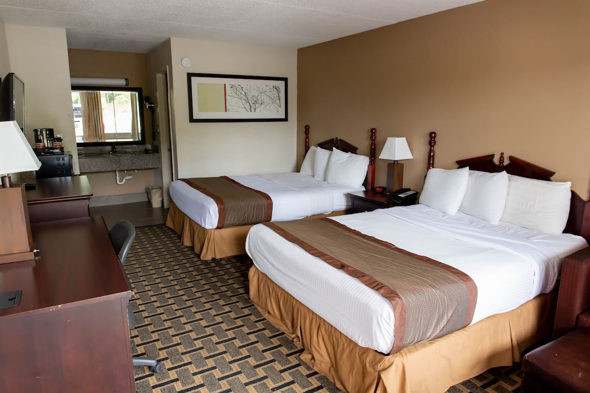 A hotel room with two beds, a desk, a chair, a lamp, and a framed picture on the wall.