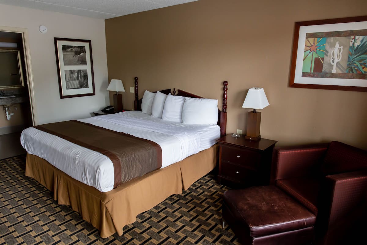 A hotel room with a large bed, two bedside tables with lamps, a chair, and a framed picture on the wall.