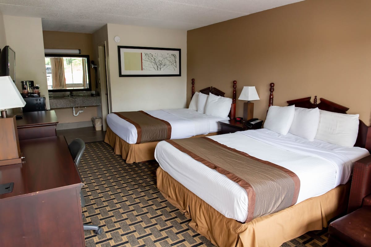 A hotel room with two beds, a desk, a chair, a bathroom, and a window.