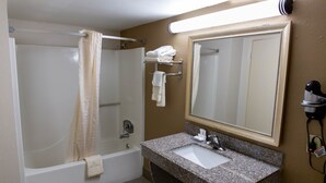 A bathroom with a shower, a sink, a mirror, and a towel rack. - Regency Inn (Monroeville)