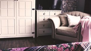 A bedroom with a bed, a dresser with drawers, a television, and a stone wall. - Beaufort House (New Ross)