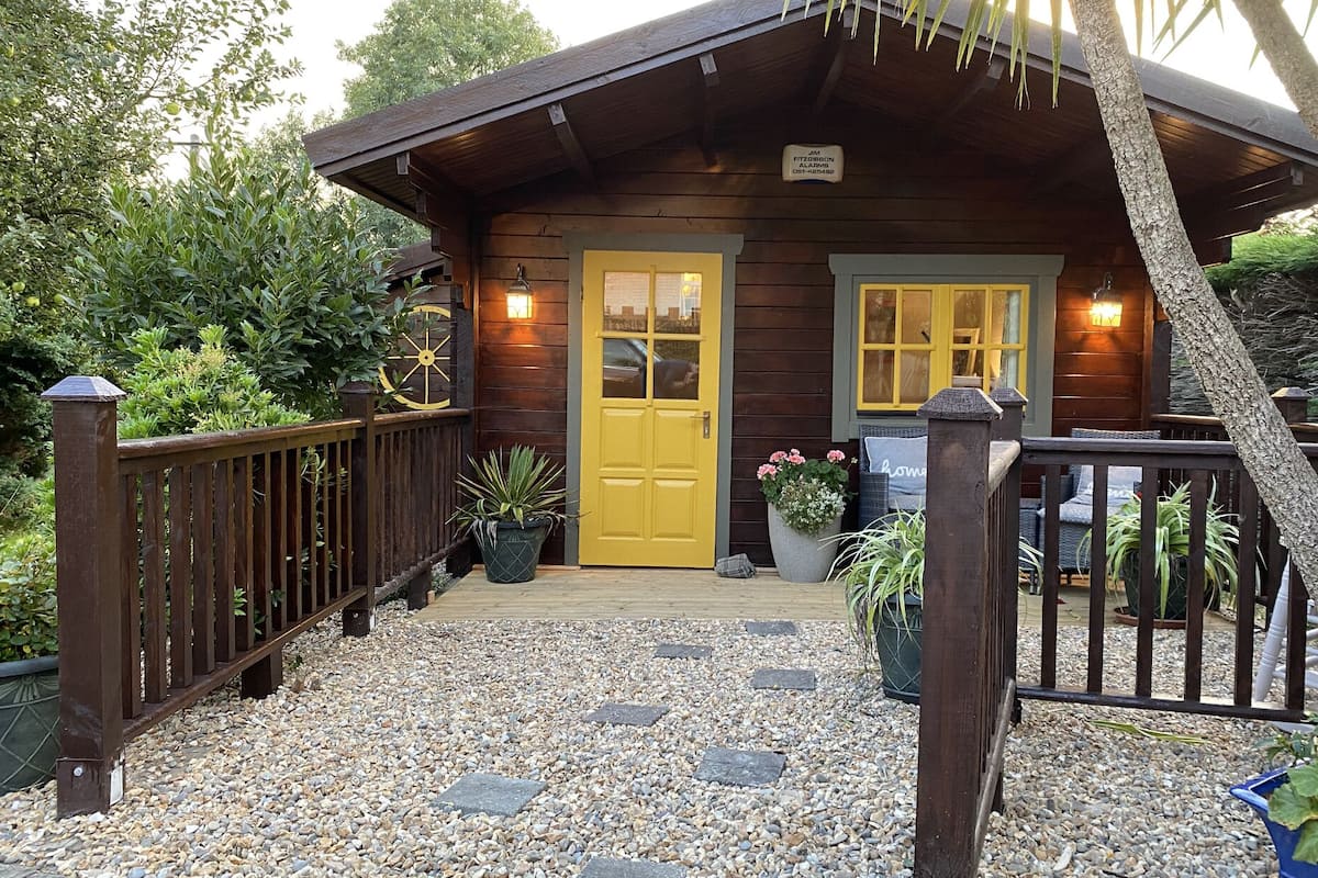 Eine Holzhütte mit gelber Tür, einem Namensschild und einem Willkommensschild.