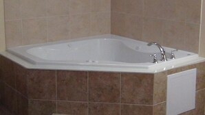 A bathroom with a freestanding bathtub, tiled walls, and a small step leading to the tub. - Voyager Inn (Aliceville)