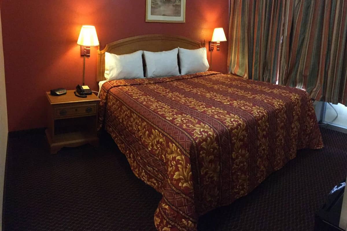 A hotel room with a large bed, two bedside lamps, a nightstand, and a painting on the wall.