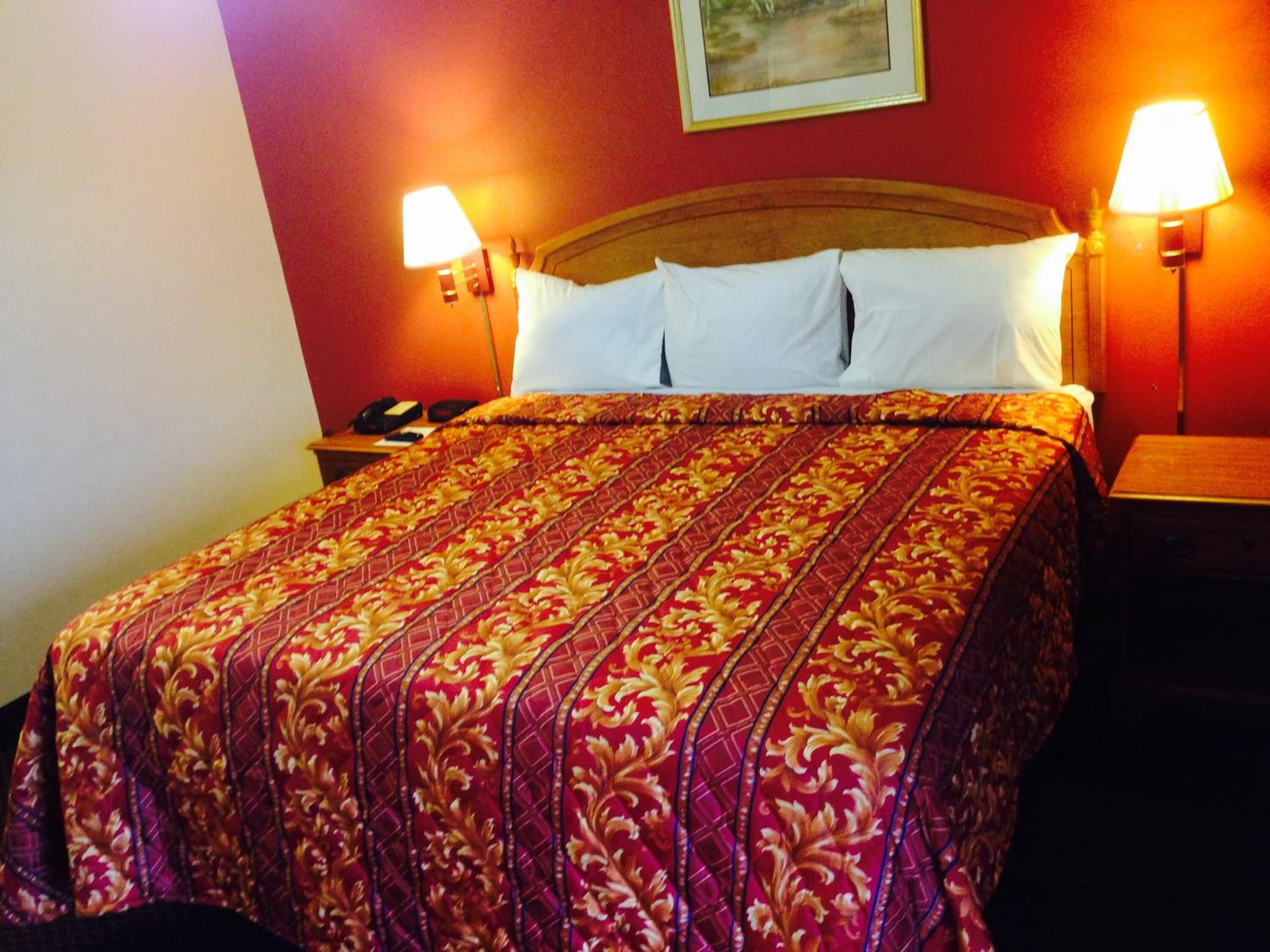 A hotel room with a large bed, two bedside lamps, and a nightstand with a phone.