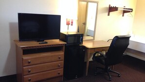 A hotel room with a wooden dresser, a television, a microwave, a desk, and a chair. - Voyager Inn (Aliceville)