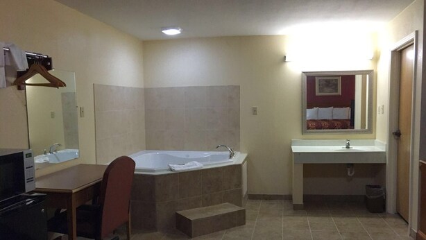 A hotel bathroom with a bathtub, a sink, a mirror, and a chair. - Voyager Inn (Aliceville)