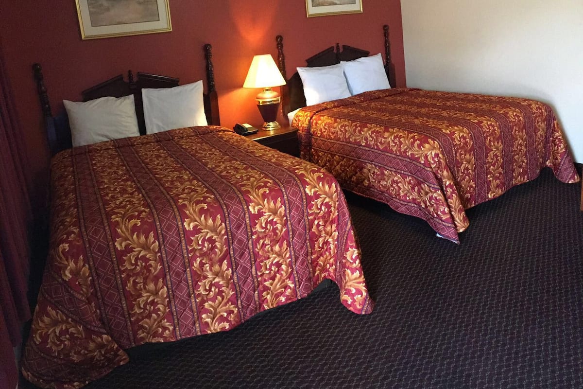 Two beds with matching red and gold bedding, a nightstand with a lamp, and two framed pictures on the wall.
