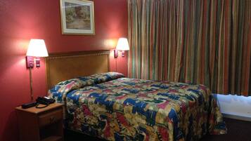 Una habitación de hotel con cabecera de madera, cubrecama estampado con flores, dos lámparas de noche, una mesita de noche y una ventana con cortinas a rayas.
