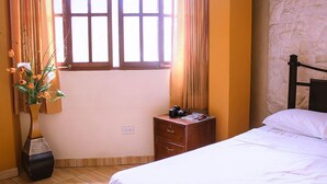 A bedroom with a bed, a nightstand, a vase with flowers, a window with curtains, and a stone wall. - Musky Hs & Suites (Chiclayo)