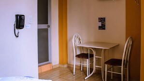 A small room with a single table and two chairs, a wall-mounted TV, a telephone, and a door with a frosted glass panel. - Musky Hs & Suites (Chiclayo)