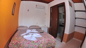 A bedroom with a floral bedspread, a bedside table, an air conditioning unit, and a sliding glass door leading to a bathroom.