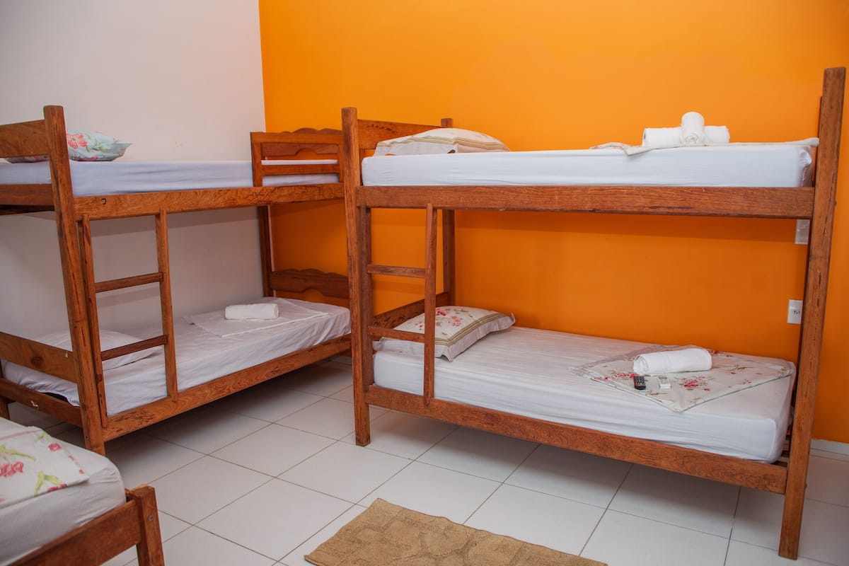 Une pièce avec trois lits superposés en bois, du linge de lit blanc et un sol carrelé.