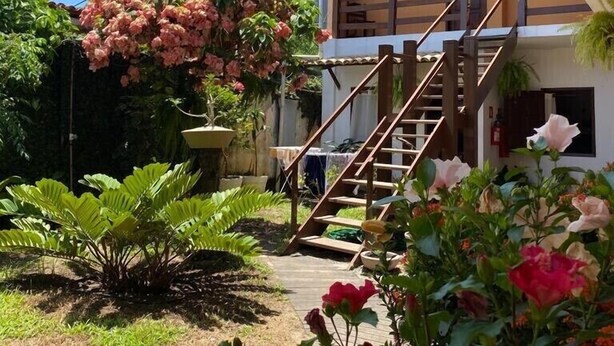 A residential property with a wooden staircase leading to a balcony, surrounded by lush greenery and flowering plants.