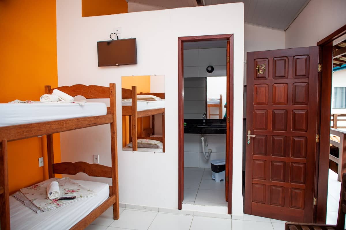 Une pièce avec des lits superposés, une porte en bois et un petit coin cuisine visible à travers une porte ouverte.