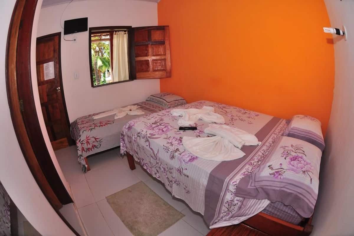 Une chambre avec deux lits, une porte en bois, une fenêtre avec des rideaux et un haut-parleur fixé au mur.