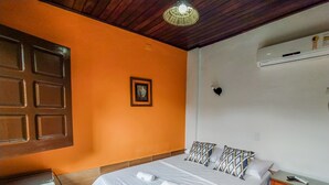 A hotel room with a bed, a nightstand, a wall-mounted air conditioner, and a small refrigerator.