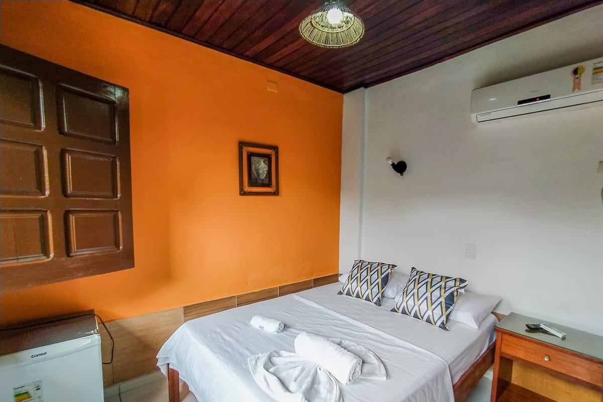 Une chambre d’hôtel équipée d’un lit, d’une table de chevet, d’un climatiseur fixé au mur et d’un petit réfrigérateur.