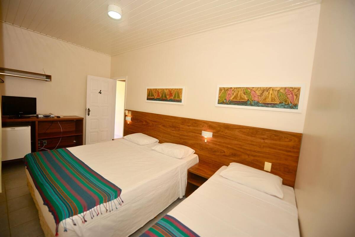Une chambre d’hôtel avec deux lits, un bureau avec une télévision et des œuvres d’art accrochées aux murs.