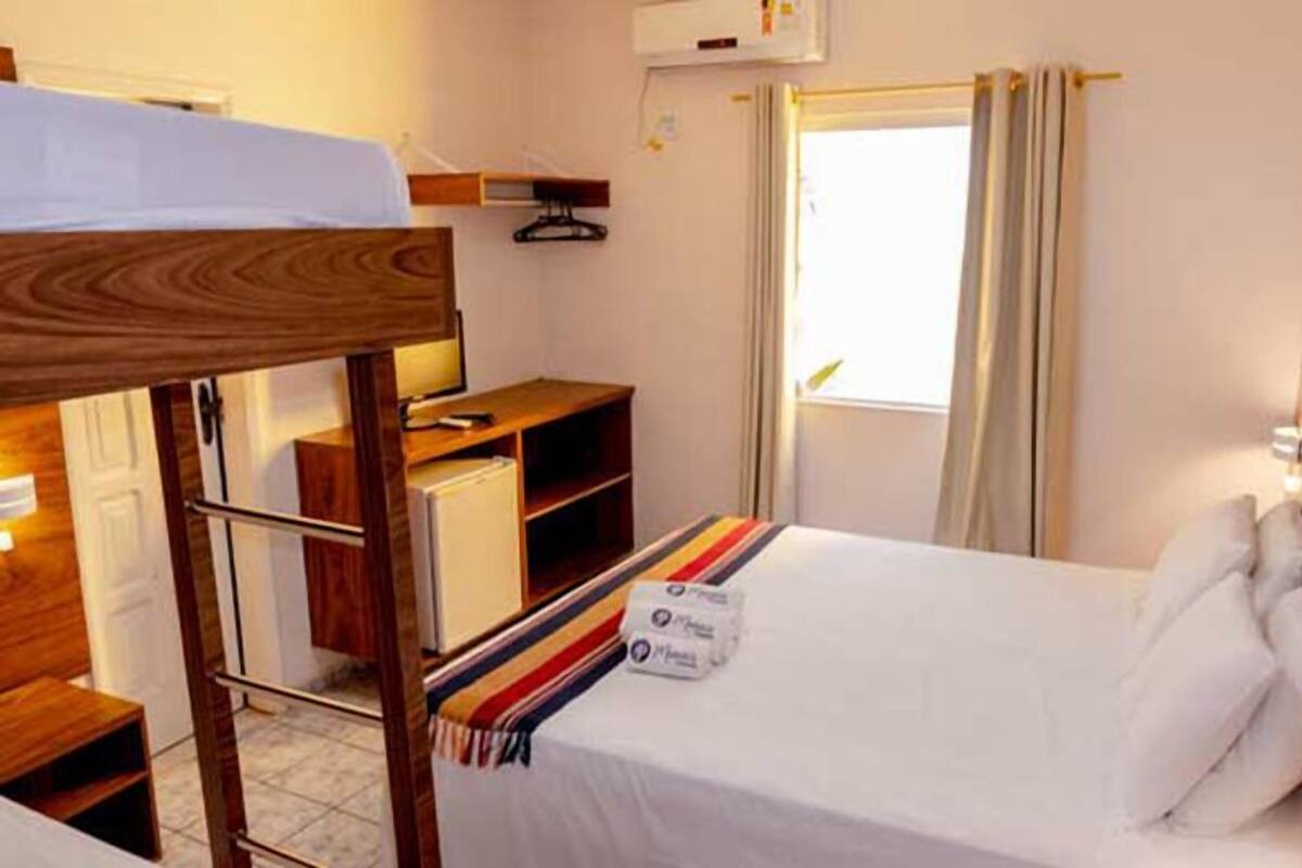 Une chambre d’hôtel compacte comprenant un lit superposé, un bureau, une chaise, une petite armoire et une fenêtre avec des rideaux.